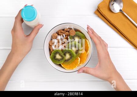 Frauen Hände halten Mehrkorn Flocken mit Orange und Kiwi Obst und Kokosnuss in Schüssel Stockfoto