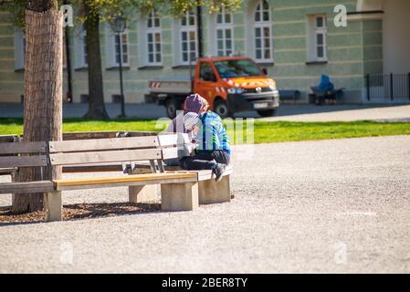 Altötting, Deutschland-April 15,2020: Eine Mutter und ihr Sohn sitzen alleine auf einer Parkbank und genießen die Sonne während der Coronavirus-Sperrmaßnahmen in Germ Stockfoto
