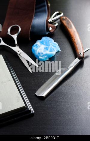 Rasiermesser, Rasierschaum, Lederwerkzeug und Schere auf schwarzem Holzhintergrund. Friseurausrüstung Stockfoto