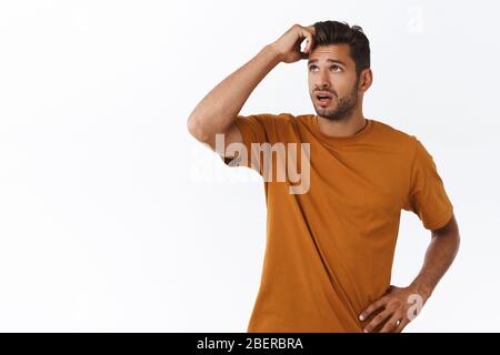 Guy versucht, Situation zu lösen, Denken Weg aus dem Problem. Attraktiver Hipster-Mann in braunem T-Shirt, Kopf kratzen und nachdenklich aufschauen, bedenken Stockfoto