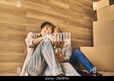 Schöner Mann und schönes Mädchen auf dem Boden hinter Pappkartons sitzen und entspannen nach dem Umzug in neue Wohnung. Stockfoto