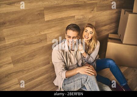 Schöner Mann und schönes Mädchen auf dem Boden hinter Pappkartons sitzen und entspannen nach dem Umzug in neue Wohnung, Blick von oben. Stockfoto