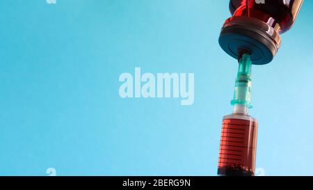 Eine Spritze ragt aus einer roten Flüssigflasche. Isoliert auf blauem Hintergrund. Medizin, Injektionen, Impfstoffe und Einwegspritzen, Drogenkonzept. Ster Stockfoto