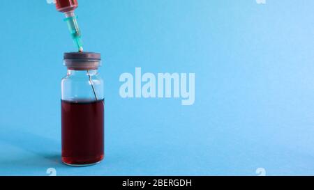 Eine Spritze ragt aus einer roten Flüssigflasche. Isoliert auf blauem Hintergrund. Medizin, Injektionen, Impfstoffe und Einwegspritzen, Drogenkonzept. Ster Stockfoto