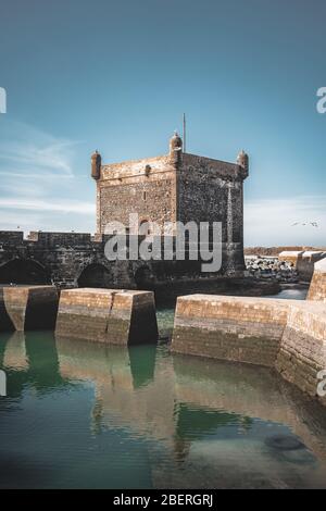 Sqala du Port, ein Verteidigungsturm am Fischereihafen von Essaouira, Marokko in der Nähe von Marrakesch. Blauer Himmel mit Wolken und Blick auf den Strand. Stockfoto