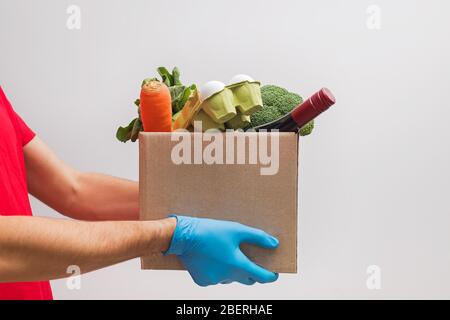 Lieferung Mann trägt Maske und Handschuhe halten Handwerk Papierbox voller verschiedener Lebensmittel. Stockfoto