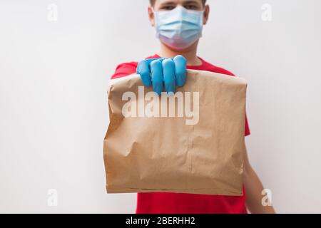 Kurier trägt Schutzhandschuhe und Maske hält Papiertüte mit Lebensmitteln Stockfoto