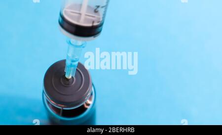 Eine Spritze ragt aus einer roten Flüssigflasche. Isoliert auf blauem Hintergrund. Medizin, Injektionen, Impfstoffe und Einwegspritzen, Drogenkonzept. Ster Stockfoto