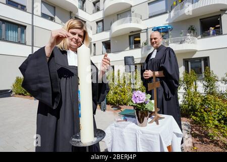 Mannheim, Deutschland. April 2020. Nina Roller, evangelische Pfarrerin, zündet während eines Gottesdienstes im Atrium des protestantischen Pflegeheims ThomasCarree eine Kerze an. Thilo Müller, protestantieller Pastor, ist auf der rechten Seite des Bildes. Quelle: Uwe Anspach/dpa/Alamy Live News Stockfoto