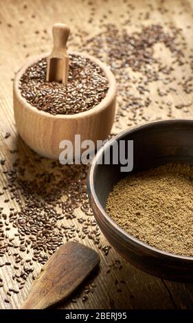 Leinsamen grobes Mehl in einer Tonschale mit Leinsamen Holzschale in der Nähe auf rustikalem Holz mit Korn rundum, Nahaufnahme, Kopierraum, gesund vegan Stockfoto