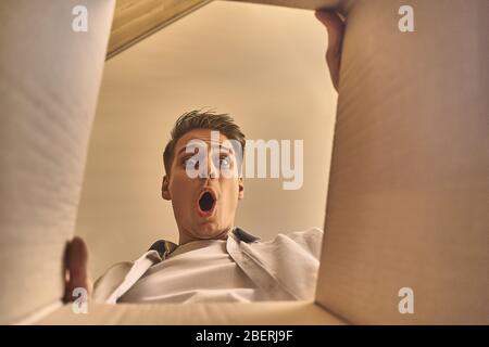 Schöner kaukasischer, stilvoller Mann, der nach dem Umzug in eine neue Wohnung einen Karton öffnet. Stockfoto