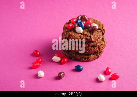 Hausgemachte Hafer Schokolade Cookies Stack mit Getreide mit saftigen Gelee Bohnen auf minimalem rosa lila Hintergrund, Winkel Ansicht Stockfoto