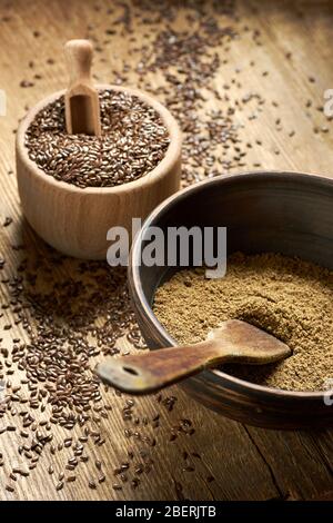 Leinsamen grobes Mehl in einer Tonschale mit Leinsamen Holzschale in der Nähe auf rustikalem Holz mit Korn rundum, Nahaufnahme, Kopierraum, gesund vegan Stockfoto