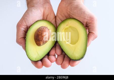 Zwei Seiten eines offenen Avocado in zwei Händen gehalten, ist der Avocado-Stein sichtbar. Avocado ist eine beliebte und gesunde Frucht reich an Nährstoffen, Vitaminen Stockfoto
