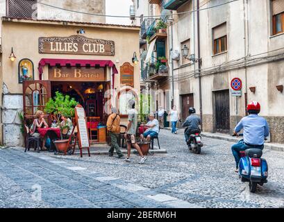 Leute sitzen in einer Bar in Cefalu, Italien mit Verkehr in der Nähe Stockfoto