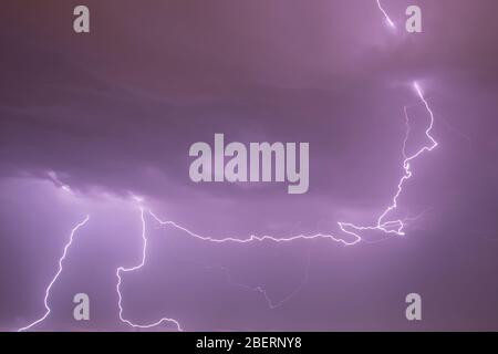 Geforked Blitz aus einem stürmischen Himmel mit elektrischer Aktivität. Himmel in lila (Magenta) Farbe. Stockfoto