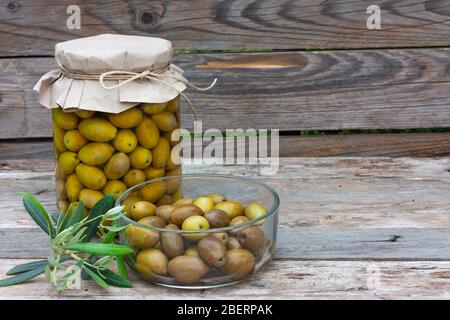 Konservierte fermentierte Oliven in Glas und Schüssel auf Holzhintergrund geschnitten. EinKonservenprodukte für Gemüse. Gesunde hausgemachte Speisen. Stockfoto
