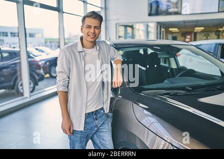 Stilvoller Mann hinter einem neuen Auto im Showroom. Stockfoto