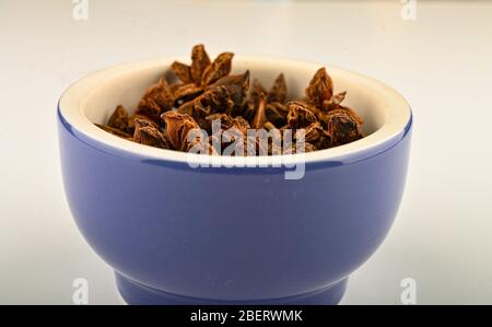 Sternanis in einem blauen keramischen Gewürzmörtel auf weißem Hintergrund. Nahaufnahme Stockfoto