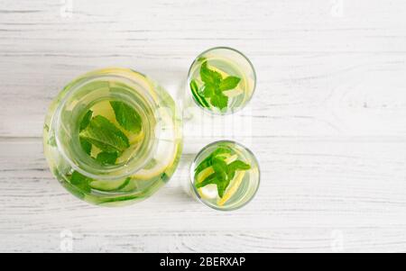 Draufsicht von Licht und frische Gurke, Zitrone und Minze trinken in Glas und Gläser auf weißem Tisch. Detox-Wasser. Stockfoto