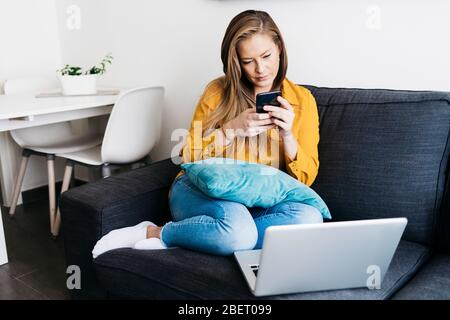 Schöne Erwachsene Frau sitzt auf dem Sofa, während mit dem Smartphone Stockfoto