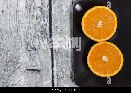 Orangefarbene Scheiben auf einem schwarzen Teller auf einem Holzhintergrund Stockfoto