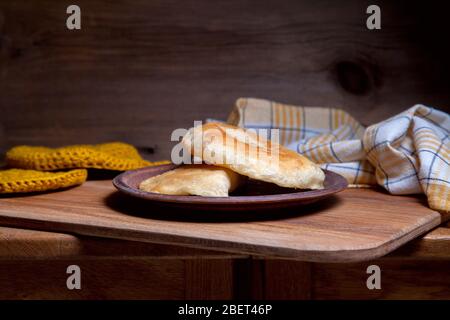 Tonplatte mit zwei einzelnen gebratenen Pasteten mit Fleisch auf Holztisch. Tatarische traditionelle Pasteten. Stockfoto