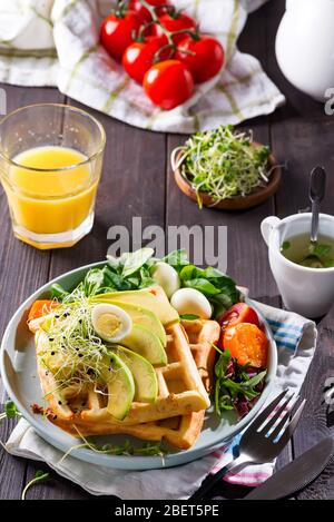 Frühstückszeit. Waffel mit Salat, Ei, Saft und Avocados zum Frühstück. Holzhintergrund Stockfoto