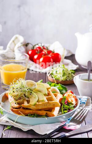 Frühstückszeit. Waffel mit Salat, Ei, Saft und Avocados zum Frühstück. Holzhintergrund Stockfoto