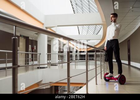 Der junge Geschäftsmann reitet auf einem gyroboard. Er spricht auf dem Smartphone Stockfoto