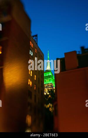 Das Empire State Building leuchtet in der Dämmerung in Midtown Manhattan New York City NY USA am 2018. Oktober in der grünen Farbe zwischen den Gebäuden. Stockfoto