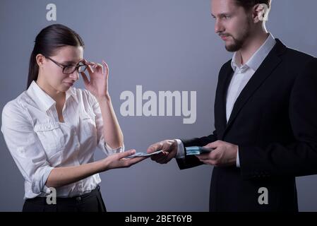 Porträt von zwei jungen Geschäftsleuten in Business-Kleidung. Eine Geschäftsfrau zieht ihre Brille aus, schaut traurig auf das kleine Gehalt, das ihr Chef einbringt Stockfoto