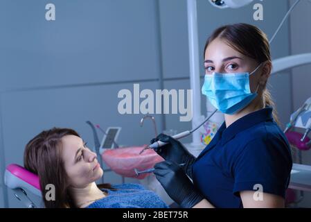 Porträt eines Zahnarztes, in einer medizinischen Maske, hält ein zahnmedizinisches Werkzeug in der Hand, der Patient sitzt in einem Stuhl. Der Arzt schaut auf die Kamera. Preventio Stockfoto