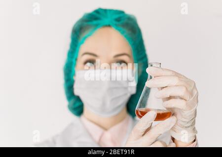 Konzept der Medizin und des Gesundheitswesens, COVID-19 . Seriöse Ärztin Virologe hält in den Händen Glas chemische Flasche mit roter Flüssigkeit. Entwicklung von