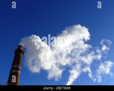 Rohre einer alten Fabrik werfen Wolken von giftigem weißem Rauch in den Himmel, die die Atmosphäre schädigen. Urbaner Smog aus Rauch aus Kesselhäusern. Weißer Rauch aus einem Kamin gegen einen blauen klaren Himmel. Stockfoto