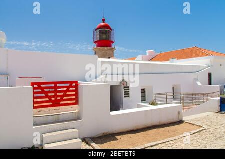 Portugal, Algarve, Kap von St. Vincent im Sommer, weißer roter Leuchtturm, rotes Holztor auf einem weißen Gebäude, klarer blauer Himmel über dem Leuchtturm, hell Stockfoto