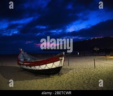 Portugal, Dämmerung über Nazare im Juni, rotes Holzboot, traditionelle portugiesische Fischerboote in Nazare, Panoramablick auf den Leuchtturm des Nazar Stockfoto