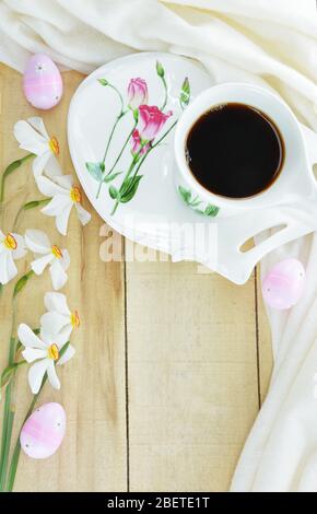 Dekorierte Ostereier, eine Tasse schwarzen Kaffee und Narcissus-Blumen des Dichters auf einem Holztisch Stockfoto
