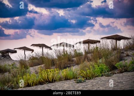 Schöne Reihe von Sonnenschirmen auf einem Sandstrand, Sonnenuntergang Wolken im Hintergrund, Stockfoto