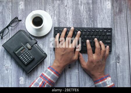 Aus einem hohen Winkel sehen Sie, wie ein Mann auf der Tastatur auf dem Schreibtisch tippt Stockfoto