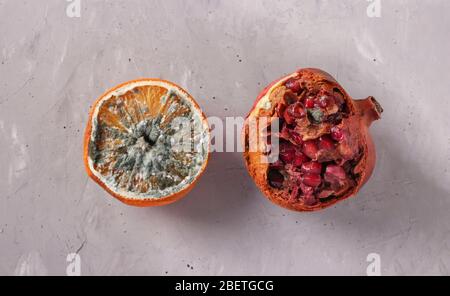 Verdorbene faule Speisen mit Schimmel: Halbe Orange und Granatapfel auf grauem Hintergrund, Draufsicht Stockfoto