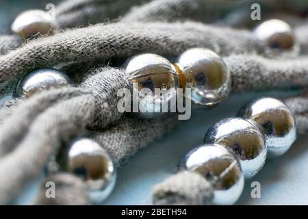 Weihnachten, Winter oder Schmuck Hintergrund. Handgefertigte graue Strickfäden mit verwitterten und zerkratzten Silberperlen auf blauem Hintergrund. Stockfoto