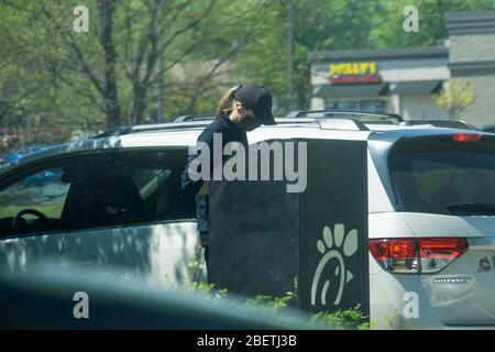 Kennesaw, GA / USA - 04/02/20: Junge, Jugendliche Fast-Food-Mitarbeiterin bei Chick-fil-A fährt mitten durch Autos und nimmt Aufträge mit Tablet entgegen. Stockfoto