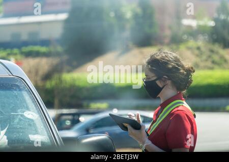 Kennesaw, GA / USA - 04/02/20: Junge, Jugendliche Fast-Food-Mitarbeiterin bei Chick-fil-A fährt mitten durch Autos und nimmt Aufträge mit Tablet entgegen. Stockfoto