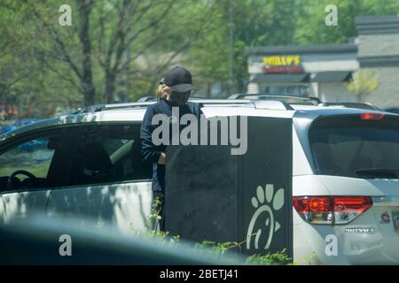 Kennesaw, GA / USA - 04/02/20: Junge, Jugendliche Fast-Food-Mitarbeiterin bei Chick-fil-A fährt mitten durch Autos und nimmt Aufträge mit Tablet entgegen. Stockfoto