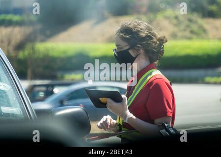 Kennesaw, GA / USA - 04/02/20: Junge, Jugendliche Fast-Food-Mitarbeiterin bei Chick-fil-A fährt mitten durch Autos und nimmt Aufträge mit Tablet entgegen. Stockfoto