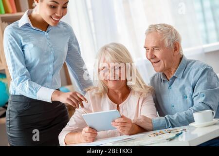 Reisebüro im Büro stehend helfen Senior Kunden sitzen Surfen Apllication auf digitalen Tablet fröhlich Stockfoto