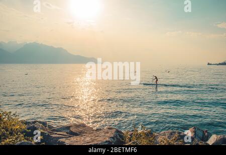 Blick auf die Alpen, Figur Silhouette eines Mannes auf einem Surfbrett mit Paddel auf dem Genfer See in Montreux, Schweizer Riviera, Kanton Waadt, Stockfoto