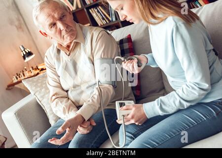 Vater und Tochter in der Bibliothek zu Hause sitzende Frau, die die Manschette aufbläht und den Blutdruck misst Stockfoto