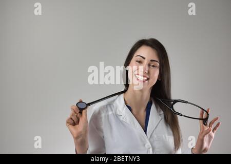 Weibliche medizinische professionelle Halten Stethoskop um den Hals isoliert auf grauem Hintergrund. Attraktive junge Frau mit schönem Lächeln. Stockfoto